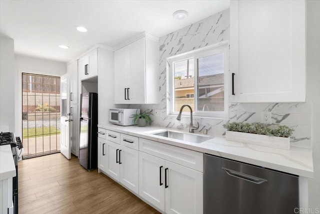 kitchen with light wood finished floors, light stone countertops, appliances with stainless steel finishes, white cabinets, and a sink