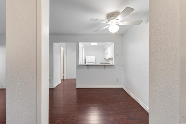 empty room with dark wood-style floors, a ceiling fan, and baseboards