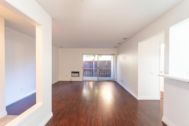 empty room with baseboards, dark wood finished floors, and heating unit