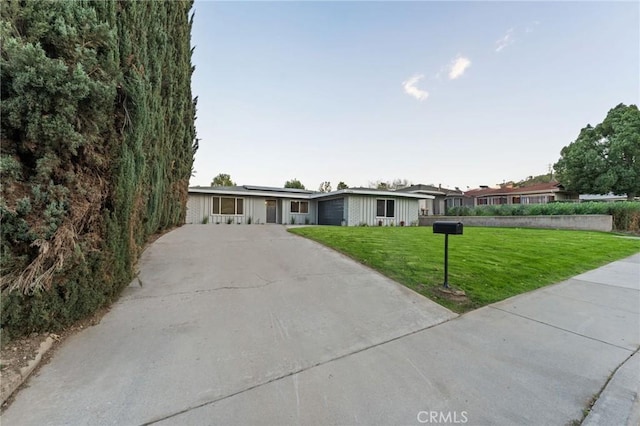 ranch-style house featuring driveway, an attached garage, solar panels, and a front yard