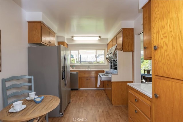 kitchen featuring brown cabinetry, tile counters, stainless steel appliances, and light wood finished floors