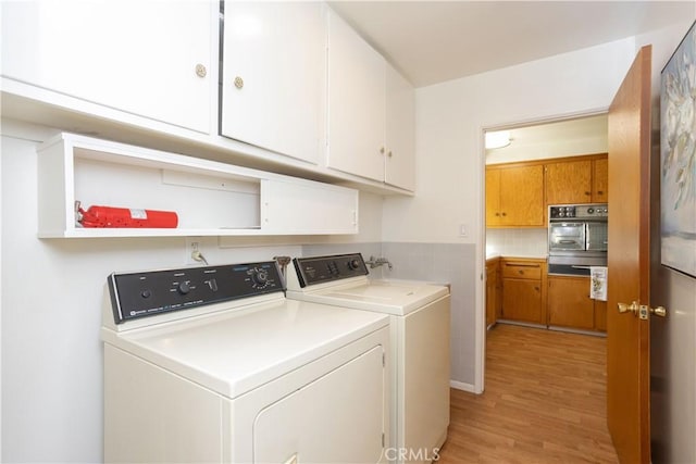 laundry area featuring light wood-type flooring, cabinet space, and independent washer and dryer