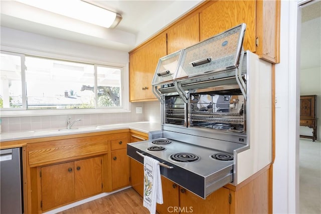 kitchen featuring light wood finished floors, tasteful backsplash, dishwasher, brown cabinets, and light countertops