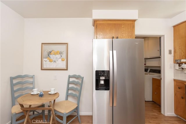 kitchen with light wood finished floors, brown cabinetry, independent washer and dryer, and stainless steel fridge with ice dispenser