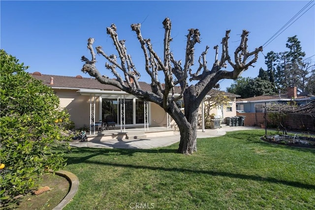 rear view of property featuring a patio area, a yard, and stucco siding