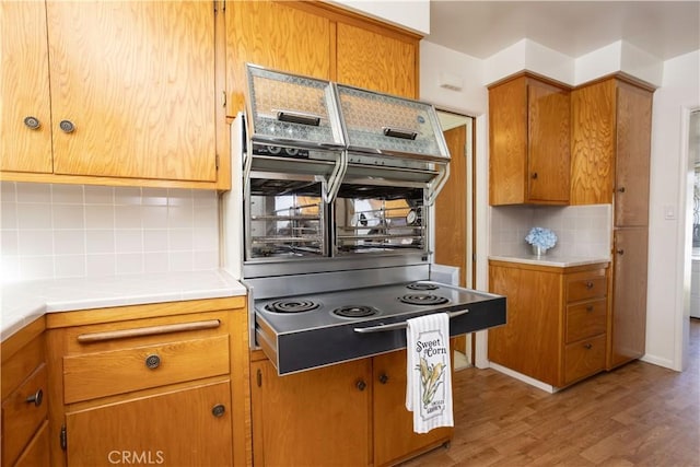 kitchen featuring brown cabinetry, wall oven, backsplash, and wood finished floors