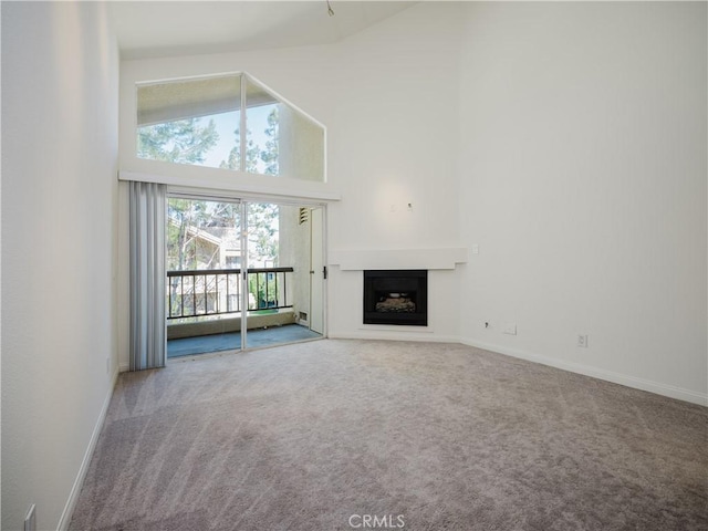 unfurnished living room featuring carpet, baseboards, a fireplace, and a high ceiling