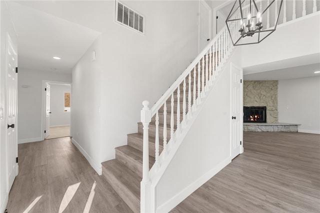 staircase featuring baseboards, visible vents, wood finished floors, and a stone fireplace