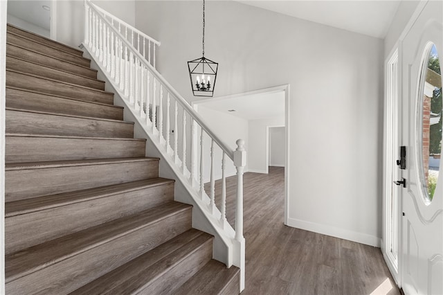 foyer featuring high vaulted ceiling, a notable chandelier, wood finished floors, baseboards, and stairway