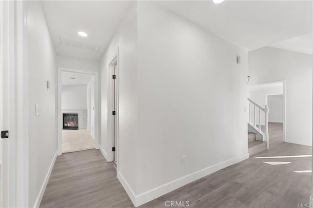 hallway featuring baseboards, stairs, visible vents, and wood finished floors