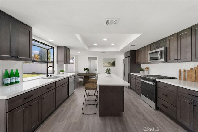 kitchen with visible vents, a tray ceiling, stainless steel appliances, dark brown cabinets, and a sink