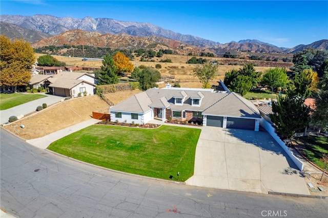 view of front of property with a tile roof, concrete driveway, an attached garage, a mountain view, and a front lawn