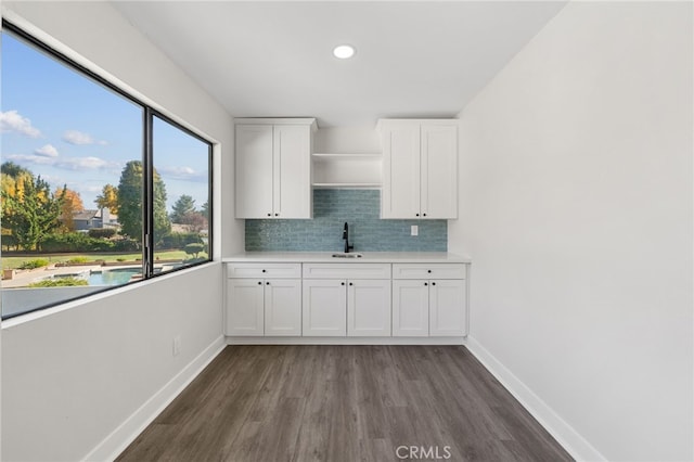 kitchen featuring dark wood-style flooring, tasteful backsplash, light countertops, white cabinets, and baseboards