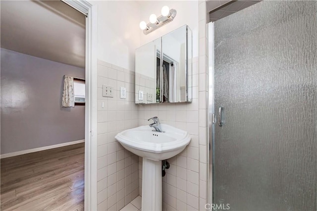 full bathroom with tile walls, a sink, a shower stall, wood finished floors, and baseboards