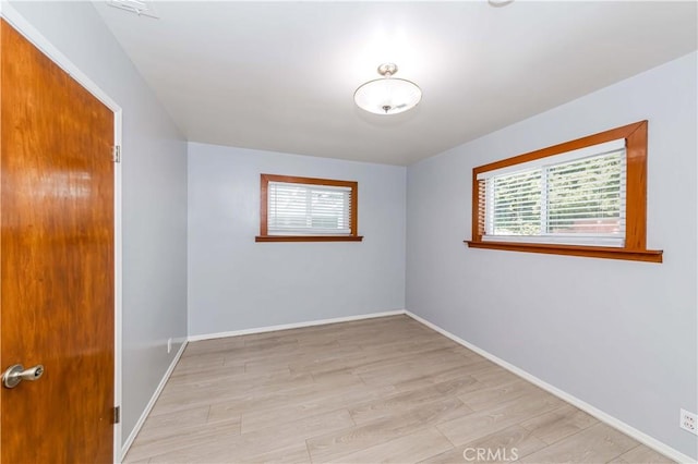 empty room featuring a healthy amount of sunlight, light wood finished floors, and baseboards