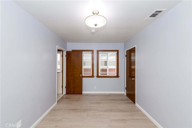 hall with light wood-style floors, baseboards, and visible vents