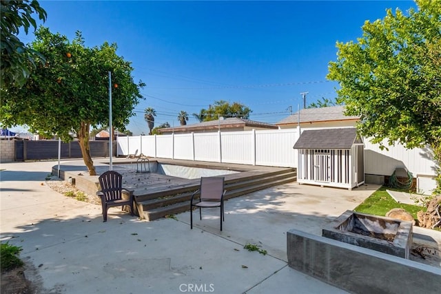 view of patio / terrace with a fenced backyard, an outdoor structure, a fire pit, and a shed