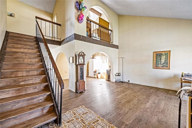 stairs with lofted ceiling, a textured ceiling, arched walkways, and wood finished floors