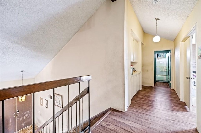 corridor with lofted ceiling, wood-type flooring, and a textured ceiling