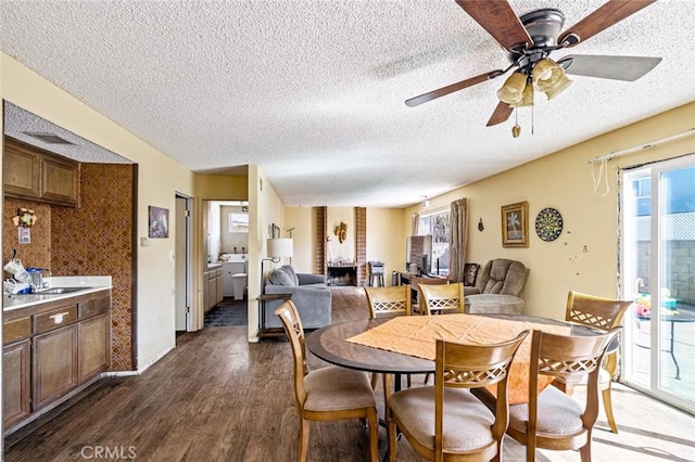 dining area with a textured ceiling, ceiling fan, a fireplace, and dark wood finished floors