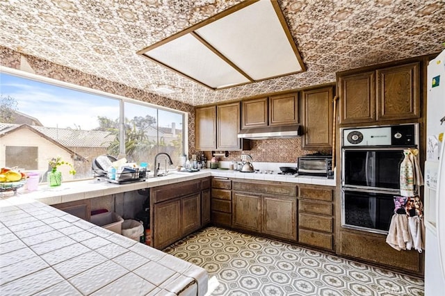 kitchen with under cabinet range hood, tile counters, a wealth of natural light, and dobule oven black