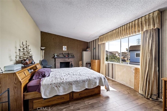 bedroom with vaulted ceiling, a textured ceiling, a brick fireplace, and wood-type flooring