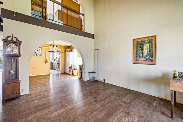 living room featuring arched walkways, visible vents, a towering ceiling, wood finished floors, and a chandelier