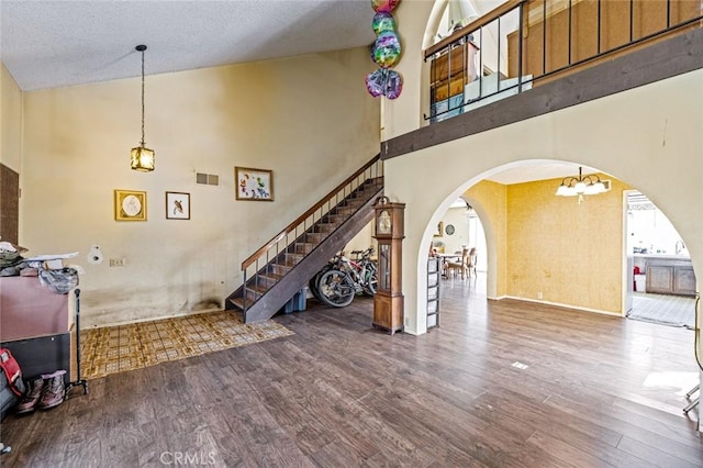 living room featuring arched walkways, visible vents, stairway, wood finished floors, and high vaulted ceiling