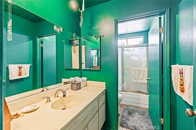 full bathroom featuring a textured wall, combined bath / shower with glass door, vanity, and toilet