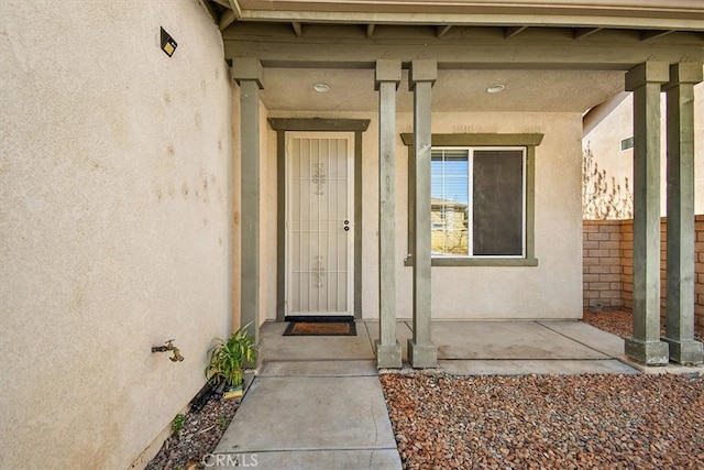 view of exterior entry featuring fence and stucco siding