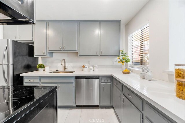 kitchen with gray cabinets, a sink, appliances with stainless steel finishes, range hood, and light countertops