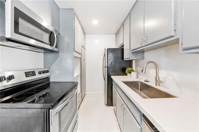 kitchen featuring appliances with stainless steel finishes, a sink, light countertops, baseboards, and light tile patterned flooring