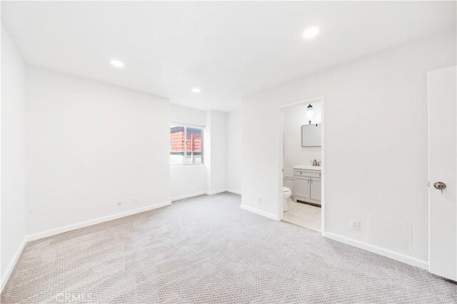 unfurnished bedroom with light carpet, recessed lighting, baseboards, connected bathroom, and a sink