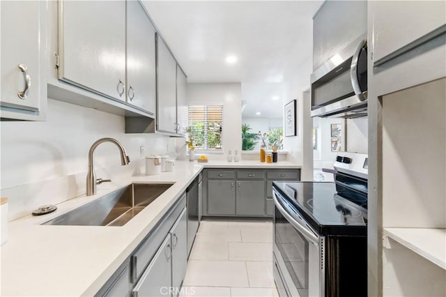 kitchen featuring appliances with stainless steel finishes, gray cabinetry, a sink, light countertops, and light tile patterned floors