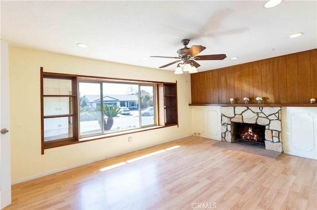 unfurnished living room featuring light wood-type flooring, a fireplace, wooden walls, and ceiling fan