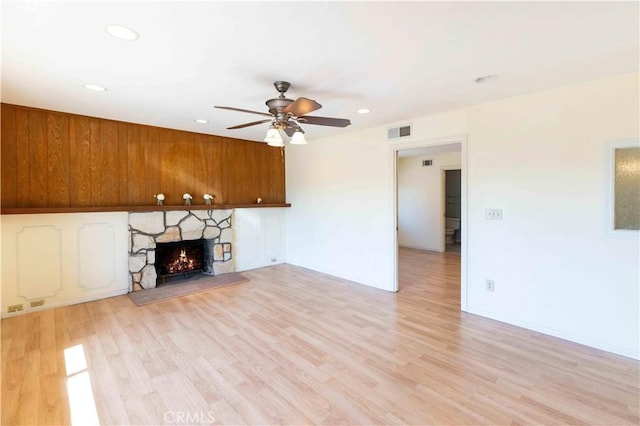 unfurnished living room with light wood-style flooring, visible vents, a ceiling fan, and a stone fireplace