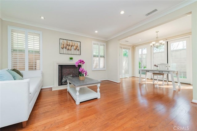 living area with a fireplace with raised hearth, light wood-style flooring, recessed lighting, visible vents, and ornamental molding