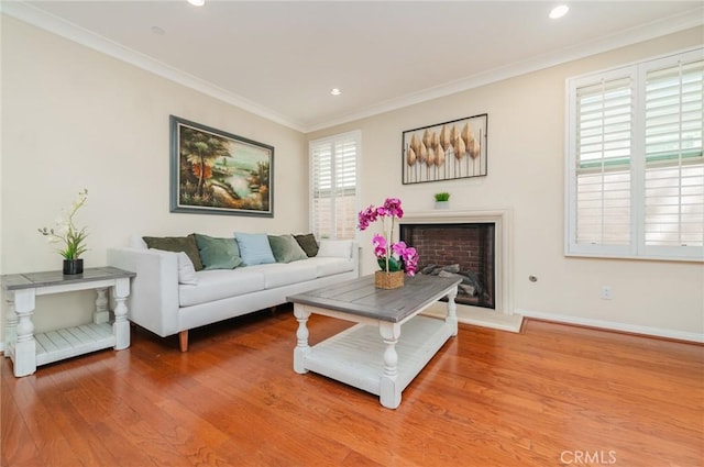 living area with a fireplace with raised hearth, recessed lighting, wood finished floors, baseboards, and crown molding