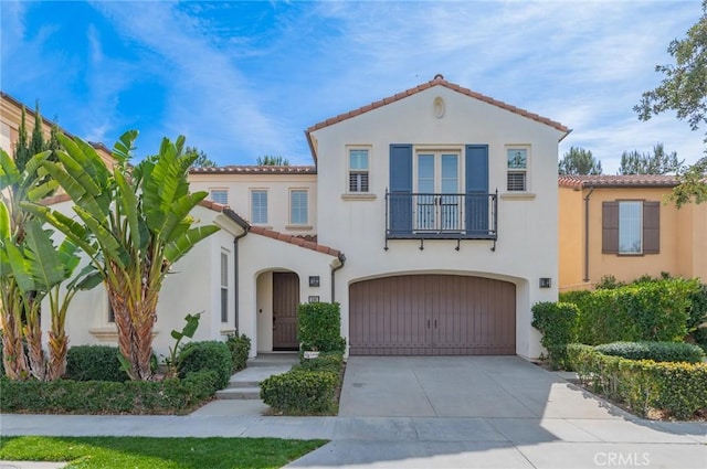 mediterranean / spanish home with a tile roof, stucco siding, an attached garage, a balcony, and driveway