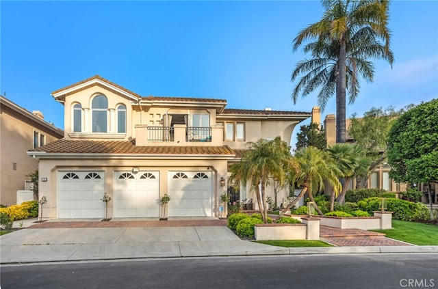 mediterranean / spanish-style home with decorative driveway, a tile roof, a balcony, and stucco siding