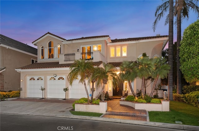 mediterranean / spanish-style home featuring a garage, driveway, a balcony, and stucco siding