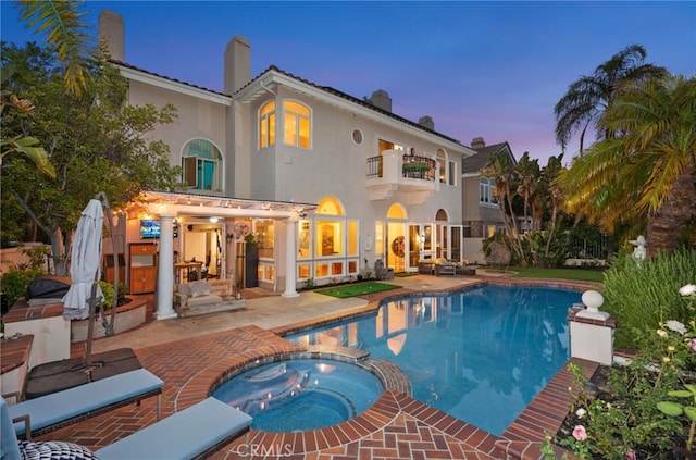 rear view of house with a patio, a balcony, a chimney, a pool with connected hot tub, and stucco siding