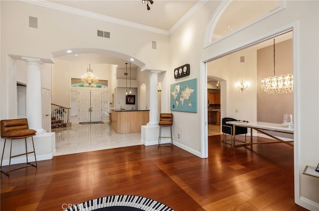 living room featuring a towering ceiling, decorative columns, visible vents, and wood-type flooring