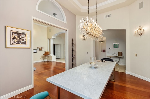 kitchen featuring arched walkways, dark wood-type flooring, visible vents, baseboards, and ornate columns