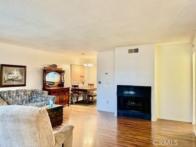 living room with a textured ceiling, a fireplace, wood finished floors, visible vents, and an inviting chandelier