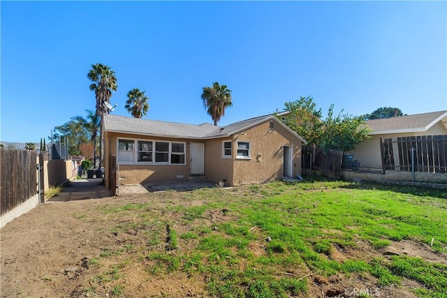 rear view of property featuring a fenced backyard, a lawn, and stucco siding