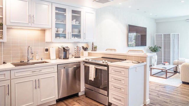 kitchen featuring white cabinets, light wood-style flooring, appliances with stainless steel finishes, a peninsula, and a sink