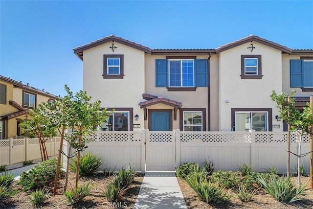 view of front of house with a fenced front yard, a tile roof, a gate, and stucco siding