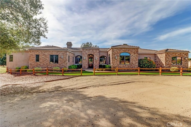 mediterranean / spanish house featuring fence, a tiled roof, stone siding, stucco siding, and a chimney