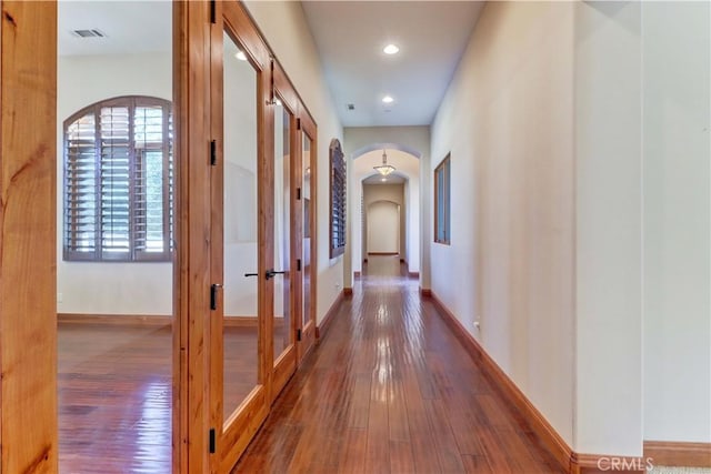 corridor featuring arched walkways, wood-type flooring, visible vents, and baseboards